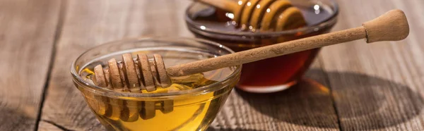 Panoramic shot of jars with honey and honey dippers on wooden table in sunlight — Stock Photo