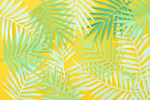 Vista superior do corte de papel folhas tropicais verdes espalhadas no fundo brilhante amarelo — Fotografia de Stock