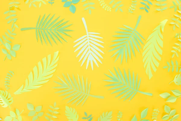 Vista superior del papel cortado hojas tropicales verdes sobre fondo amarillo brillante - foto de stock