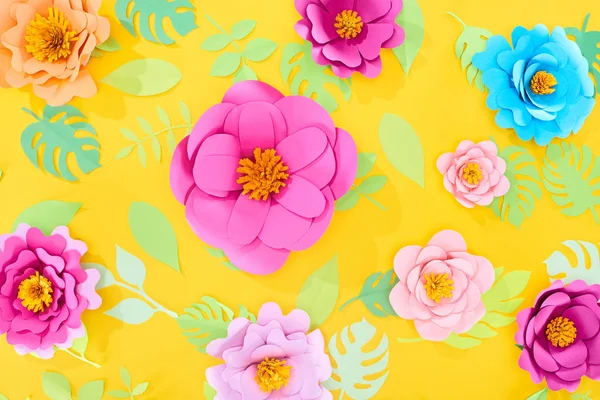Top view of paper cut flowers with green tropical leaves on yellow bright background — Stock Photo