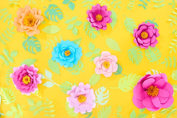 Draufsicht auf Papier geschnitten helle Blumen mit grünen tropischen Blättern auf gelbem, hellem Hintergrund — Stockfoto