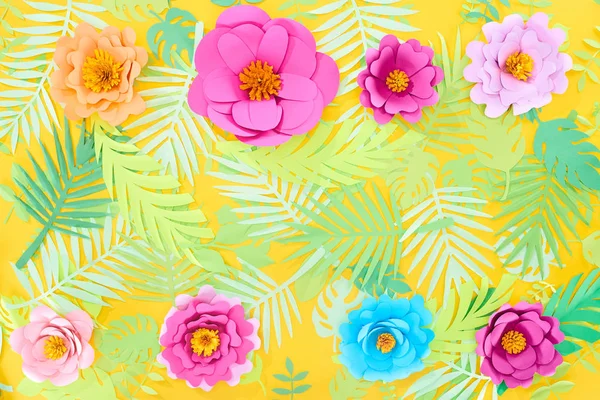 Flat lay with paper cut multicolored flowers on tropical leaves on yellow bright background with copy space — Stock Photo