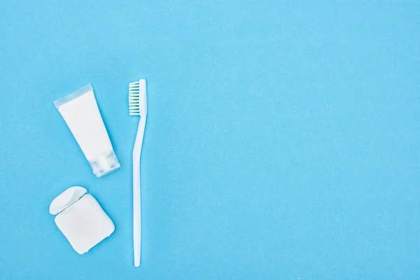Vista superior del cepillo de dientes y la pasta de dientes cerca de hilo dental aislado en azul - foto de stock