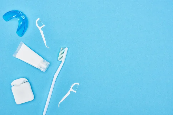 Vista superior del cepillo de dientes, pasta de dientes y hilo dental cerca de retenedor aislado en azul - foto de stock