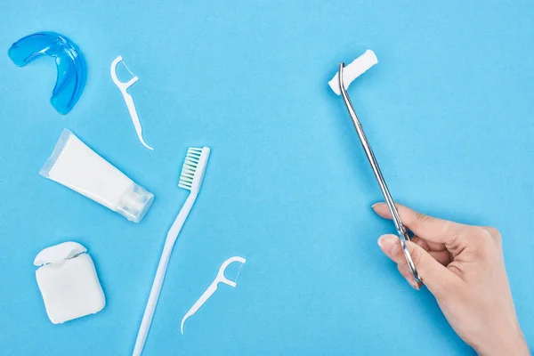 Vista cortada de mulher segurando pinças com almofada de algodão perto de pasta de dentes e escova de dentes em azul — Fotografia de Stock