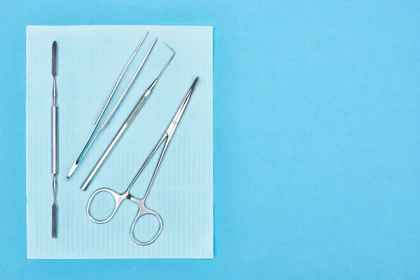 Vista superior de conjunto de acero inoxidable con herramientas dentales en delantal aislado en azul - foto de stock