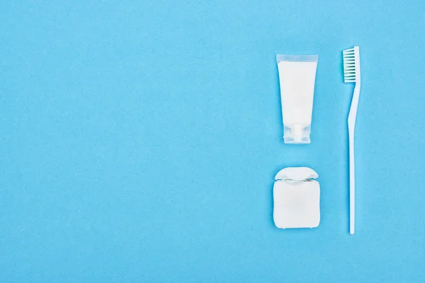 Vista superior del cepillo de dientes y la pasta de dientes cerca de hilo dental aislado en azul - foto de stock