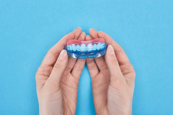 Cropped view of woman holding retainer with prosthesis in hands isolated on blue — Stock Photo