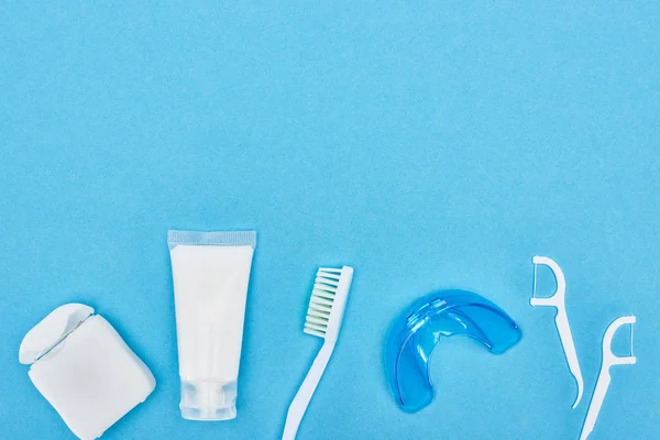 Верхний вид зубной пасты, зубной щетки и зубной нити рядом с фиксатором и зубной нитью зубочистки изолированы на синий цвет — стоковое фото