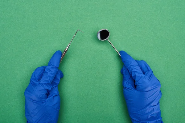 Visão recortada do dentista em luvas de látex segurando ferramentas dentárias isoladas em verde — Fotografia de Stock