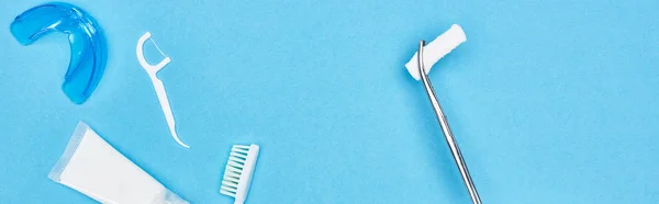 Plano panorámico de pinzas con almohadilla de algodón cerca de pasta de dientes y cepillo de dientes en azul - foto de stock