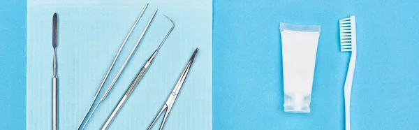 Prise de vue panoramique de l'ensemble avec des outils dentaires près de dentifrice et brosse à dents isolé sur bleu — Photo de stock