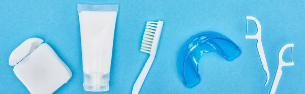 Prise de vue panoramique de brosse à dents, dentifrice et fil dentaire près de l'appareil de retenue et les bâtons de fil dentaire isolés sur bleu — Photo de stock