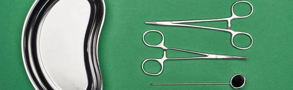 Panoramic shot of scissors and dental mirror near metallic plate isolated on green — Stock Photo