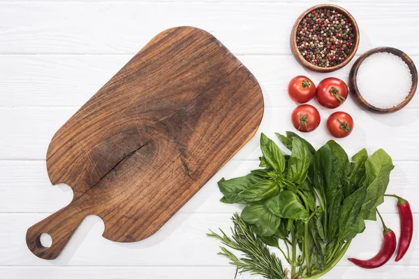 Top view of cutting board, cherry tomatoes, greenery, chili peppers, salt and spices — Stock Photo