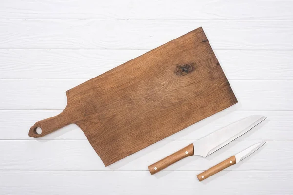 Vue du dessus de la planche à découper et des couteaux sur la table blanche — Photo de stock