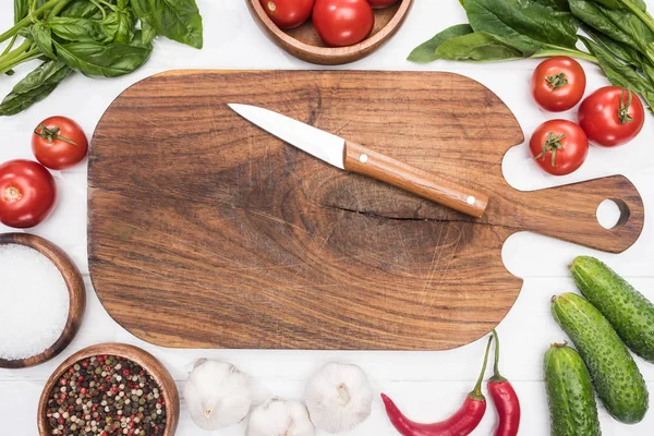 Top view of cutting board, cherry tomatoes, greenery, chili peppers, salt, garlics, knife and spices — Stock Photo