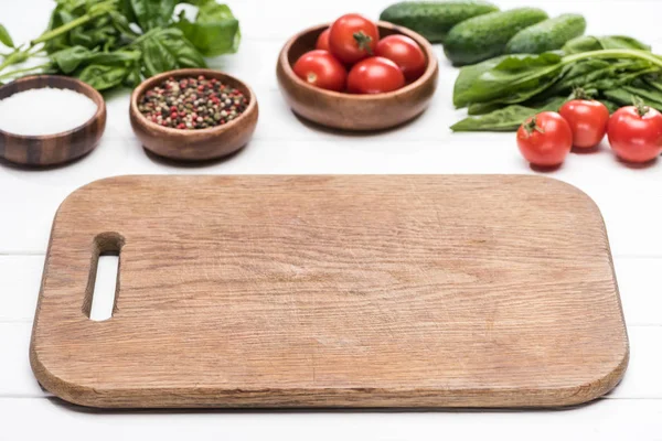 Cutting board, cherry tomatoes, greenery, cucumbers, salt and spices — Stock Photo