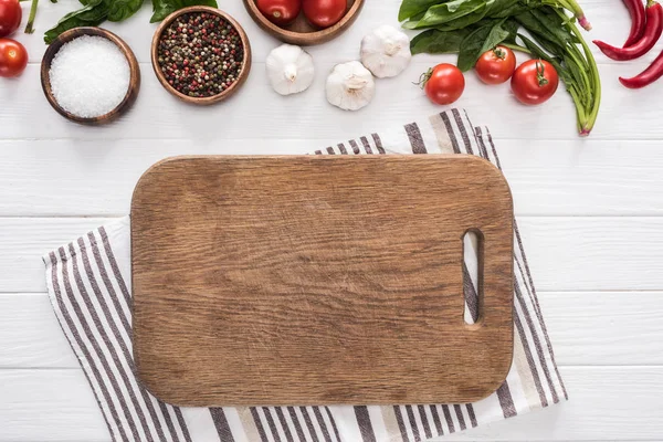 Top view of cutting board, cloth, cherry tomatoes, greenery, chili peppers, salt, garlics and spices — Stock Photo