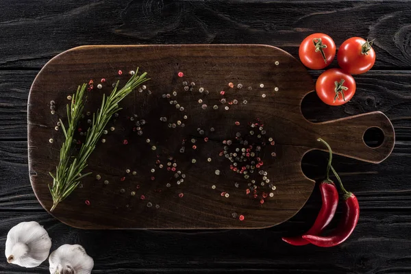 Top view of wooden cutting board with spices, greenery, cherry tomatoes, chili peppers and garlics — Stock Photo