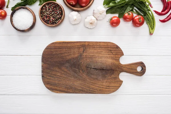Top view of cutting board, cherry tomatoes, greenery, chili peppers, salt, garlics and spices — Stock Photo