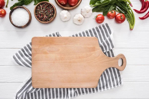 Top view of cutting board, cloth, cherry tomatoes, greenery, chili peppers, salt, garlics and spices — Stock Photo