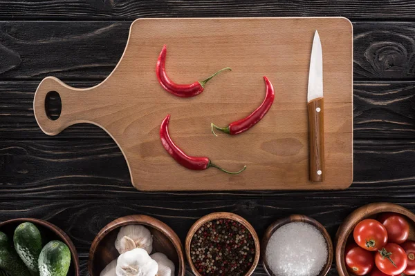 Top view of cutting board, cherry tomatoes, salt, garlics, cucumbers, knife, chili peppers and spices — Stock Photo