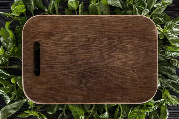Top view of wooden cutting board on leaves of basil — Stock Photo