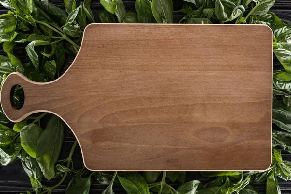 Top view of wooden cutting board on leaves of basil — Stock Photo