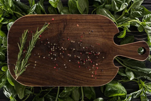 Top view of wooden cutting board with spices and rosemary on leaves of basil — Stock Photo