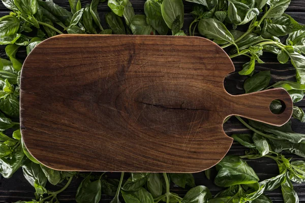 Top view of wooden cutting board on leaves of basil — Stock Photo