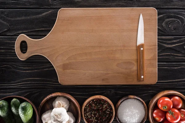 Top view of cutting board, cherry tomatoes, salt, garlics, cucumbers, knife and spices — Stock Photo