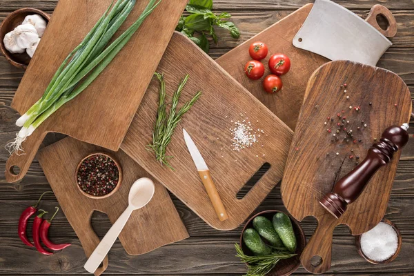 Top view of cutting boards, cherry tomatoes, salt, garlics, cucumbers, chili peppers, pepper mill, spoon, meat chopper, knife and spices — Stock Photo