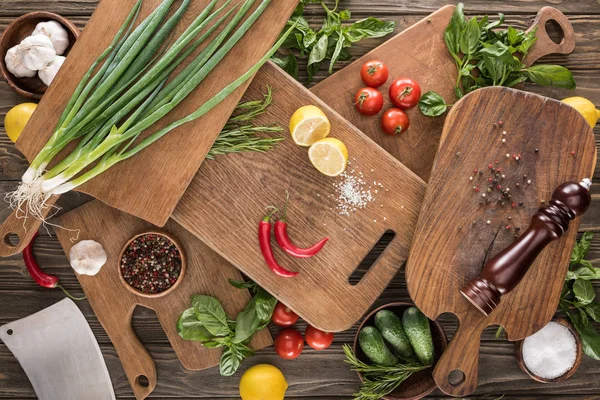 Top view of cutting boards, cherry tomatoes, salt, garlics, cucumbers, chili peppers, pepper mill, meat chopper, lemons and spices — Stock Photo