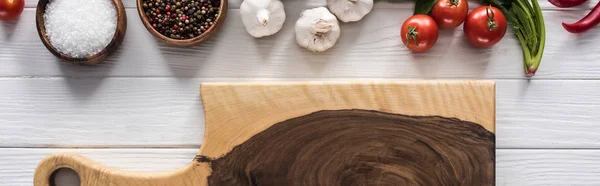 Panoramic shot of wooden chopping board, garlics, salt, cherry tomatoes, spices and greenery — Stock Photo