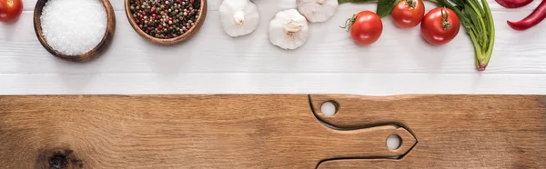 Panoramic shot of wooden chopping boards, garlics, salt, cherry tomatoes, chili peppers, spices and greenery — Stock Photo
