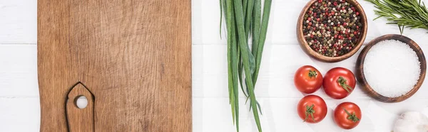 Panoramic shot of wooden chopping board, garlic, salt, cherry tomatoes, spices and greenery — Stock Photo