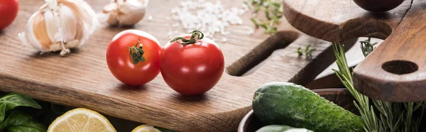 Panoramic shot of cutting boards, cherry tomatoes, salt, garlics, greenery, cucumber — Stock Photo