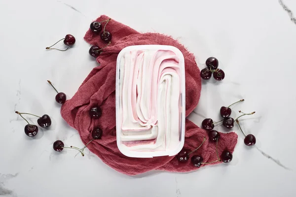 Vue du dessus de délicieuse crème glacée sur tissu rose près de cerises sur fond gris marbre — Photo de stock