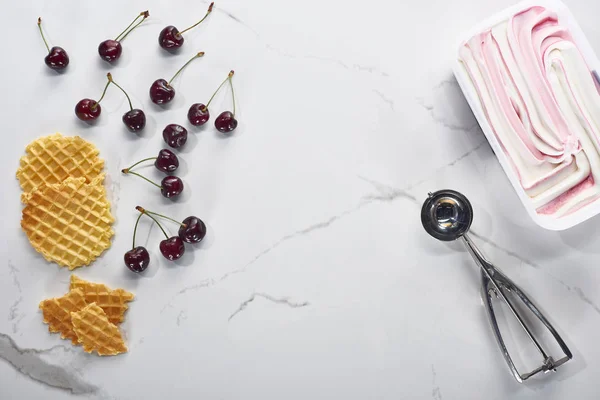 Вид сверху на вкусные вафли, ложки и вишни и мороженое на мраморно-сером фоне — стоковое фото