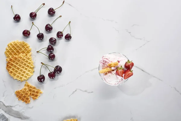 Top view of delicious ice cream with waffles and strawberries near cherries on marble grey background — Stock Photo