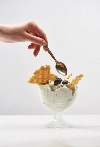 Partial view of woman holding spoon near delicious pistachio ice cream with waffles and blueberries isolated on grey — Stock Photo