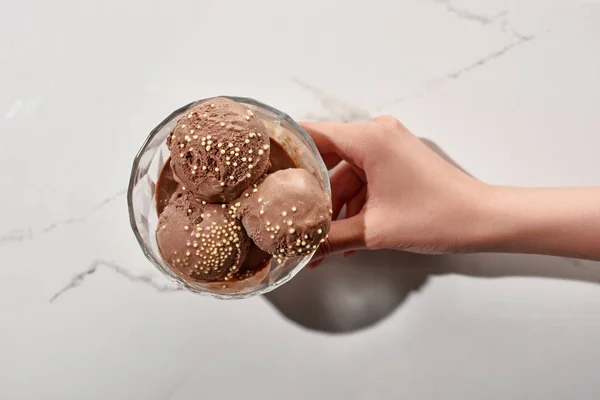 Vista cortada de mulher segurando delicioso sorvete de chocolate na tigela no fundo cinza mármore — Fotografia de Stock