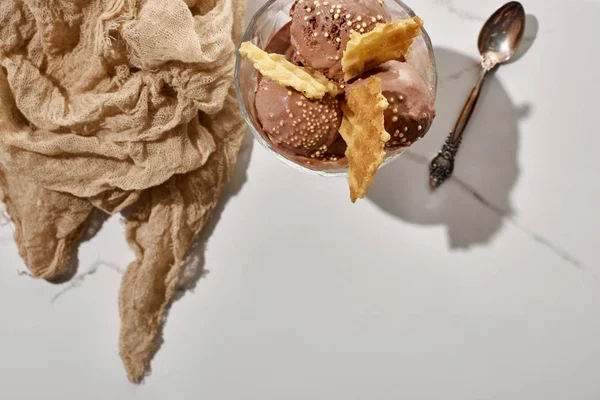 Vista dall'alto di delizioso gelato al cioccolato in ciotola con cialde vicino panno marrone e cucchiaio su sfondo grigio marmo — Foto stock