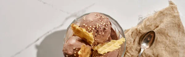 Top view of delicious chocolate ice cream in bowl with waffles near brown cloth with spoon on marble grey background, panoramic shot — Stock Photo