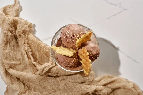 Vista superior de delicioso helado de chocolate en tazón con gofres cerca de tela marrón sobre fondo gris mármol - foto de stock