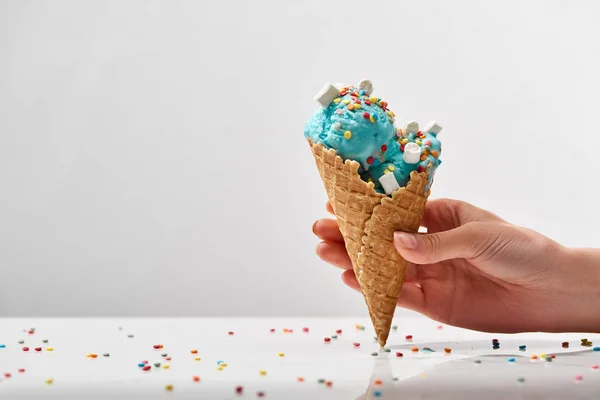 Abgeschnittene Ansicht der Frau mit köstlichen süßen blauen Eis mit Marshmallows und Streusel in knusprigen Waffelkegel isoliert auf grau — Stockfoto