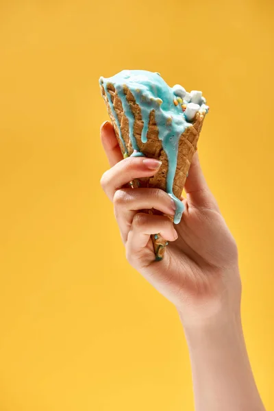 Vue partielle de la femme tenant une délicieuse crème glacée bleue fondue dans un cône de gaufre croustillant isolé sur jaune — Photo de stock