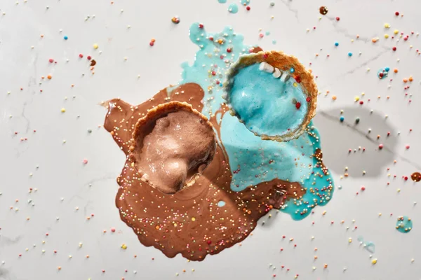 Вид сверху на вкусный расплавленный шоколад и синее мороженое в вафельных рожках на мраморно-сером фоне с брызгами — стоковое фото