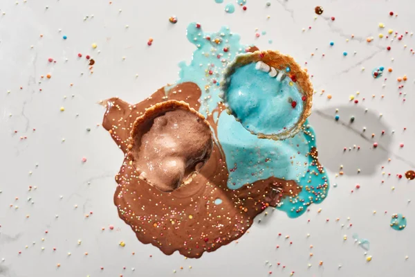 Top view of delicious melted chocolate and blue ice cream in waffle cones on marble grey background with sprinkles — Stock Photo